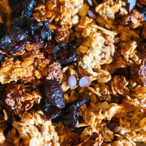 Die Schokodrops und getrockneten Früchte auf dem noch heißen Granola verteilen und gut untermischen.