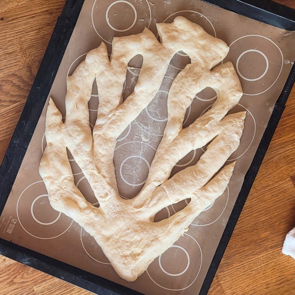 Use a dough scraper to cut a leaf pattern into the dough and carefully pull the dough further to separate it. Leave the fougasse to rest for another hour at room temperature. 