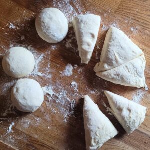 Die Teiglinge zu runden Brötchen schleifen und mit der Hand etwas flach drücken. Auf ein Backblech legen und abdecken.